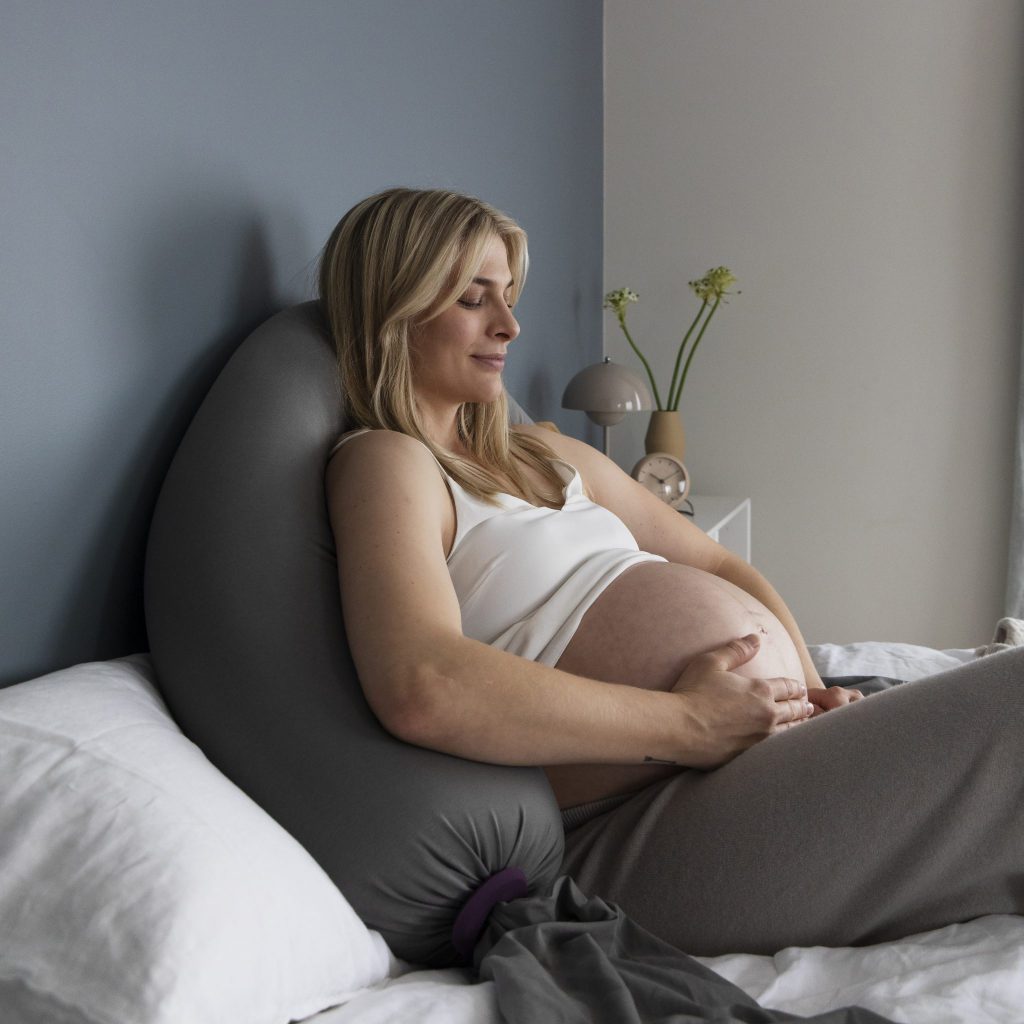 Gravid kvinne hviler i sengen med gravidepute fra bbhugme